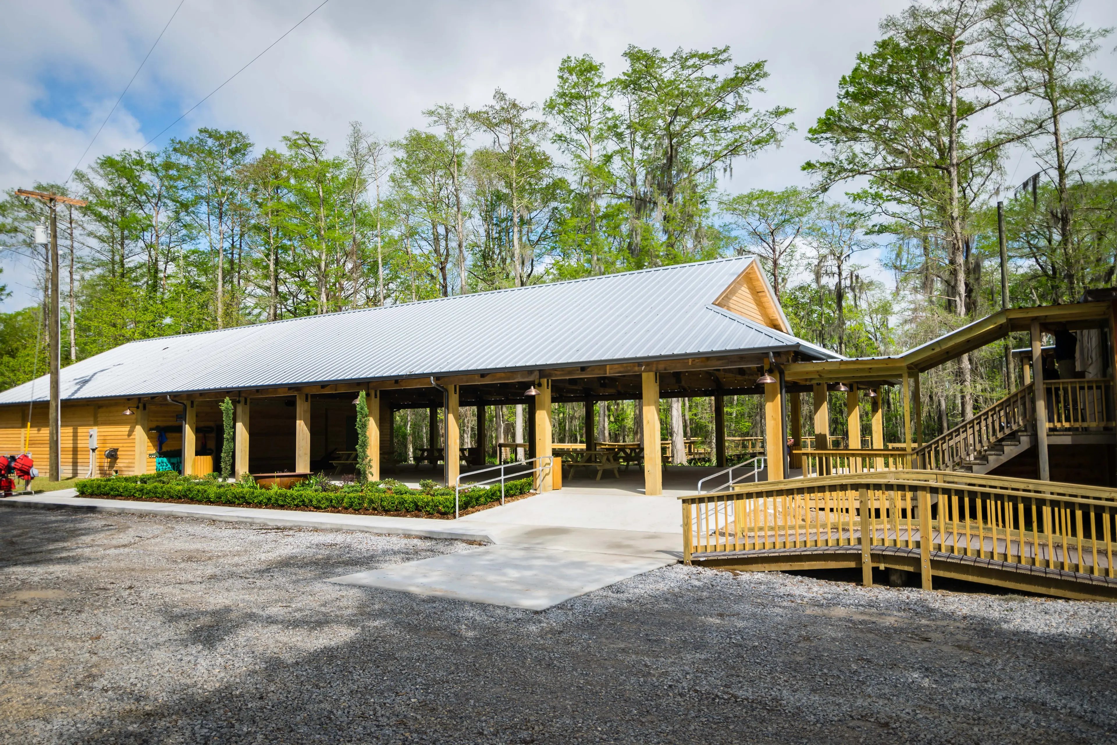 A large wooden pavilion behind a gravel parking lot.
